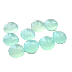 May include: A collection of ten light blue, faceted gemstones. Each gem has a rounded shape with multiple cut surfaces, creating a sparkling effect. The gems are arranged on a white background.