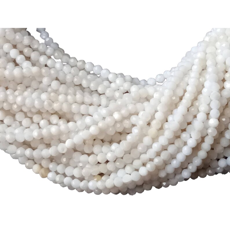 May include: A strand of white faceted gemstone beads. The beads are small and round, and they have a smooth, polished finish.
