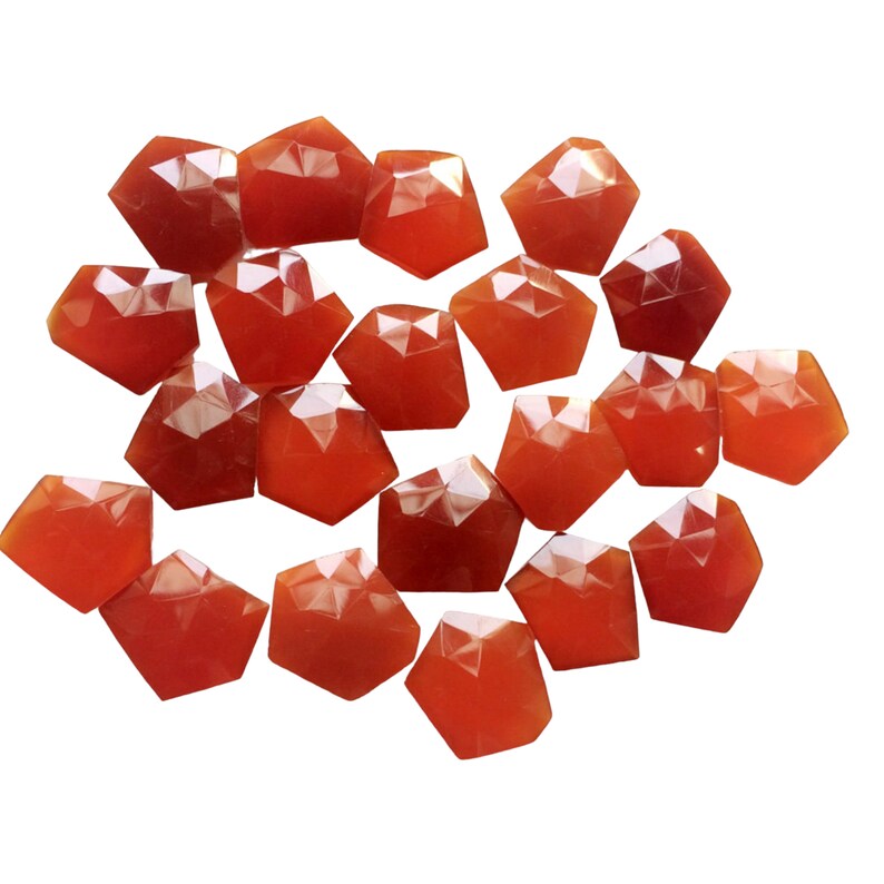 Puede incluir: Una colecci&oacute;n de 18 piedras preciosas de cornalina facetadas, cada una con una forma y un tama&ntilde;o &uacute;nicos. Las piedras son de color rojo anaranjado intenso y tienen un acabado liso y pulido.