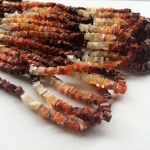May include: A strand of red, orange, and white gemstone beads. The beads are square and have a rough, natural texture.