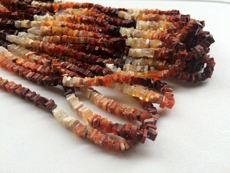 May include: A strand of red, orange, and white gemstone beads. The beads are square and have a rough, natural texture.
