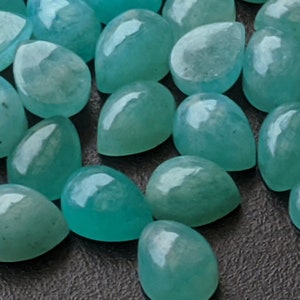 May include: A collection of loose, teardrop-shaped gemstones in a vibrant turquoise-blue color. Each stone features a smooth, polished, cabochon-style surface with a glossy finish, reflecting light across their rounded, symmetrical forms.