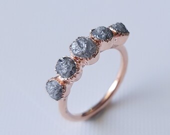May include: A rose gold band ring with five grey rough diamonds set in a row.
