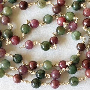May include: A silver chain necklace with green and pink beads. The beads are round and have a smooth, polished finish.