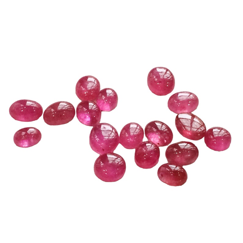 Pu&ograve; includere: Una collezione di 15 pietre preziose di colore rosso rubino, di forma ovale e tagliate a cabochon. Le pietre sono lisce e lucidate, con un leggero bagliore.