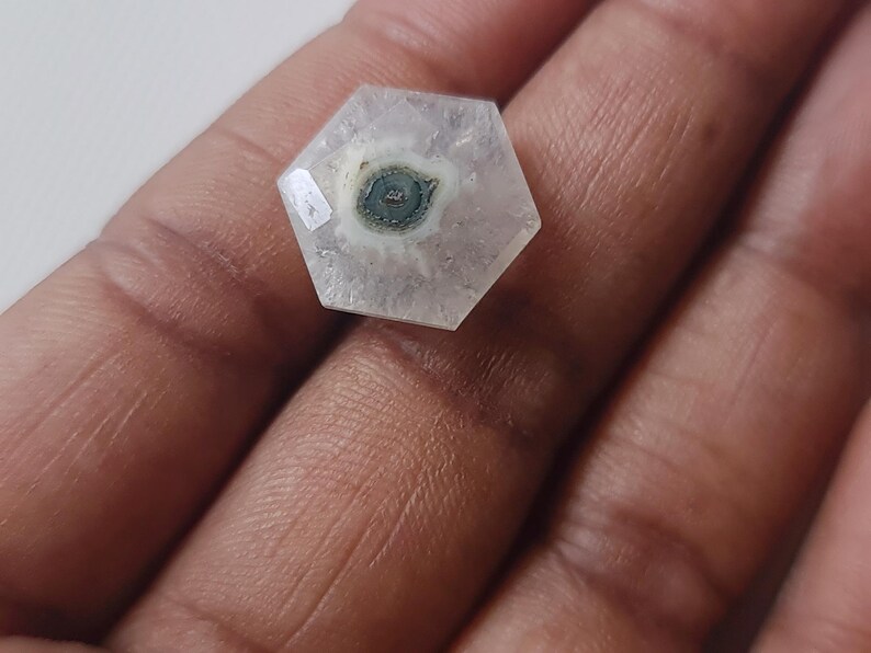 May include: A hexagonal, clear, white, and gray gemstone with a dark gray and white pattern in the center.