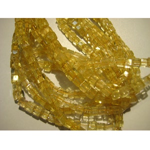 May include: A strand of yellow citrine gemstone beads, each bead is faceted and has a square shape.