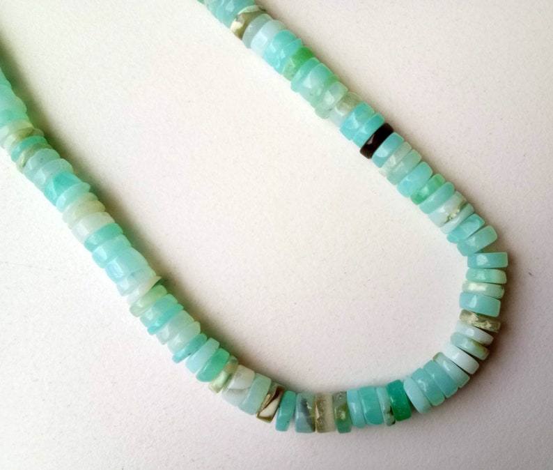 May include: A light blue opal bead necklace with a variety of sizes and shapes. The beads are strung on a clear thread and have a natural, iridescent finish.