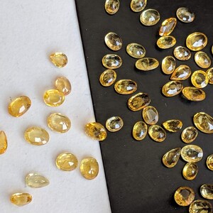 May include: A collection of yellow gemstones, some oval shaped and some teardrop shaped, scattered on a white and black background.