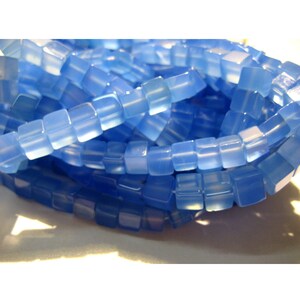 Puede incluir: Una hebra de cuentas cuadradas de color azul claro. Las cuentas son translúcidas y tienen un aspecto ligeramente esmerilado.