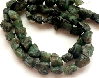 Op de afbeelding: Een streng ruwgeslepen smaragd edelstenen. De stenen variëren in grootte en vorm en vertonen een reeks donkergroene tinten. De edelstenen zijn aan elkaar geregen, waardoor een ketting of armband ontstaat.