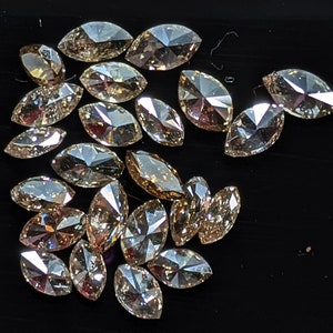 Puede incluir: Una colecci&oacute;n de diamantes de color marr&oacute;n claro de forma marquesa. Los diamantes est&aacute;n dispuestos en un mont&oacute;n suelto sobre una superficie negra.