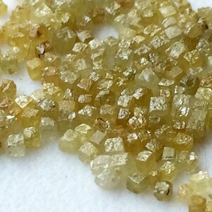 May include: A close-up of a group of small, faceted, yellow-green diamonds. The diamonds are scattered on a white surface.