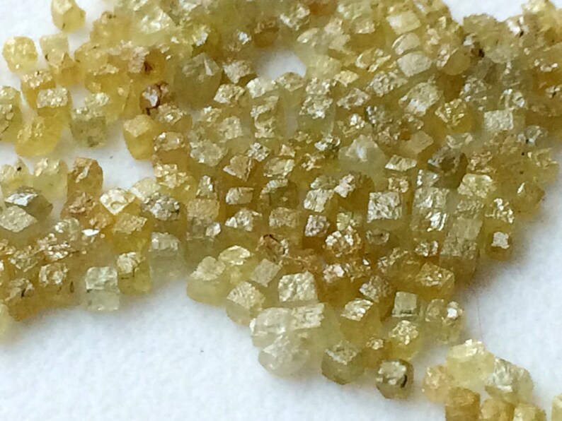 May include: A close-up of a group of small, faceted, yellow-green diamonds. The diamonds are scattered on a white surface.