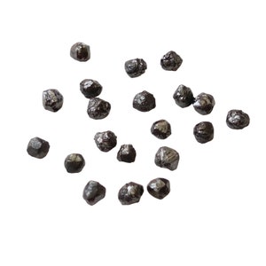 May include: A collection of small, dark grey, faceted diamonds scattered on a white background.