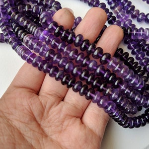 May include: A strand of deep purple amethyst beads, each bead is round and slightly faceted. The beads are strung on a clear thread and are approximately 8mm in diameter.