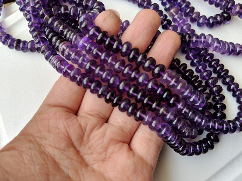 May include: A strand of deep purple amethyst beads, each bead is round and slightly faceted. The beads are strung on a clear thread and are approximately 8mm in diameter.