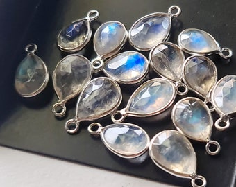 May include: A group of pear-shaped moonstone gemstone pendants with silver-toned jump rings. The stones are translucent and have a milky white color with iridescent blue and green flashes.