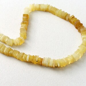 May include: A strand of yellow opal beads, each bead is a rectangular shape with a slightly irregular cut. The beads are strung on a clear thread.