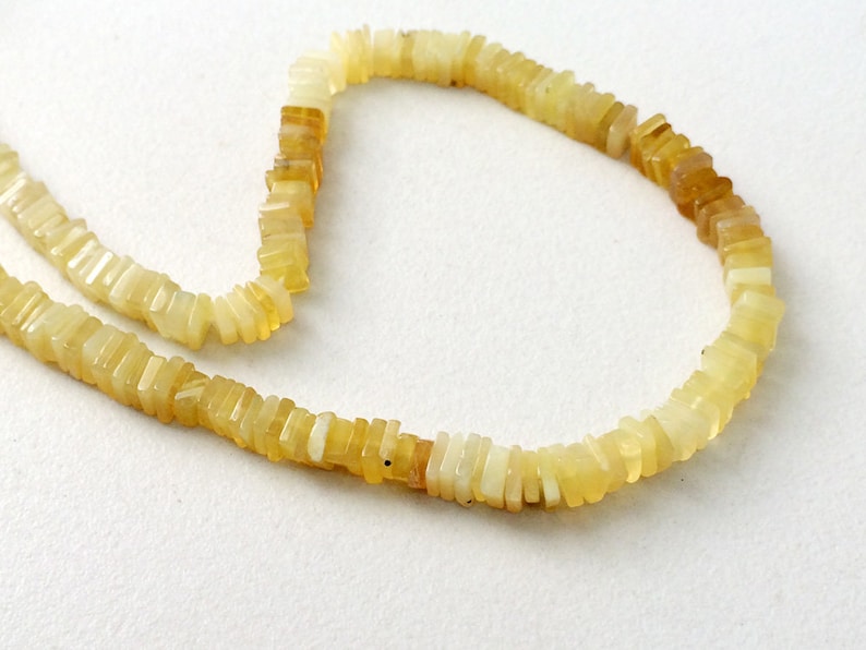May include: A strand of yellow opal beads, each bead is a rectangular shape with a slightly irregular cut. The beads are strung on a clear thread.