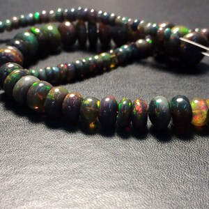 May include: A strand of black opal beads with iridescent green, blue, and gold flashes. The beads are round and have a smooth, polished finish.