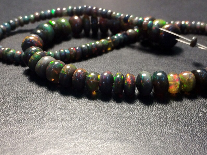 May include: A strand of black opal beads with iridescent green, blue, and gold flashes. The beads are round and have a smooth, polished finish.
