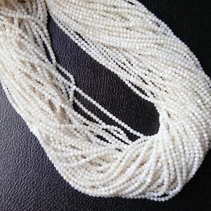 May include: A strand of white gemstone beads, likely moonstone, with a faceted finish. The beads are small and uniform in size, creating a delicate and elegant look.