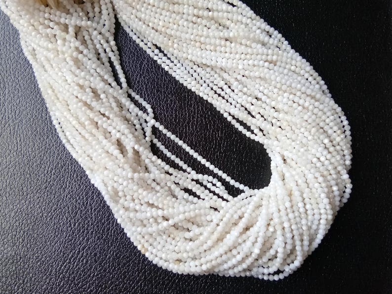 May include: A strand of white gemstone beads, likely moonstone, with a faceted finish. The beads are small and uniform in size, creating a delicate and elegant look.