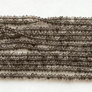 May include: A strand of gray faceted gemstone beads. The beads are small and round, and they have a slightly irregular shape. The beads are strung on a clear thread.
