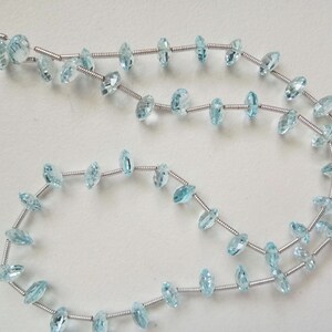 May include: A strand of light blue gemstone beads strung on silver wire. The beads are faceted and have a marquise shape.