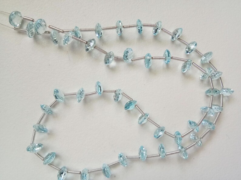 May include: A strand of light blue gemstone beads strung on silver wire. The beads are faceted and have a marquise shape.
