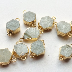May include: A collection of eight hexagonal, raw, light green gemstone pendants with gold-toned metal accents. Each pendant has two jump rings for attaching to jewellery.