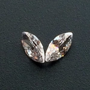 May include: Two clear marquise-shaped gemstones with a slight pink hue.