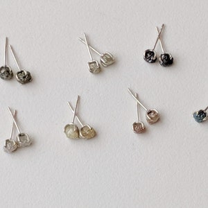May include: A set of ten silver stud earrings with raw diamond accents. The diamonds are in various shades of gray, black, and white.