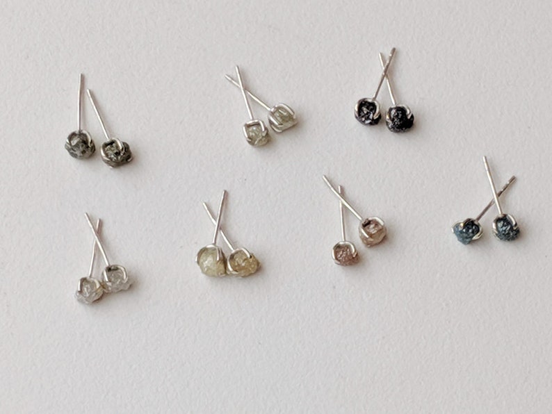 May include: A set of ten silver stud earrings with raw diamond accents. The diamonds are in various shades of gray, black, and white.