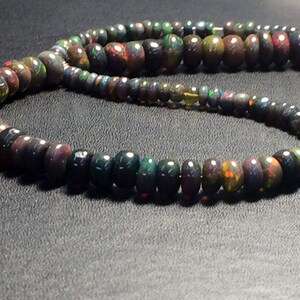 May include: A strand of black opal beads with iridescent green, red, and gold flashes. The beads are round and have a smooth, polished finish.