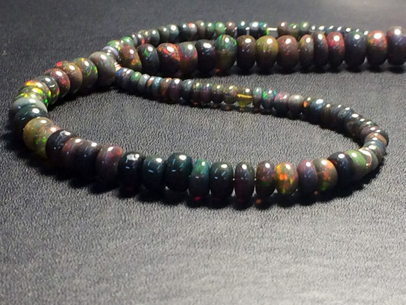 May include: A strand of black opal beads with iridescent green, red, and gold flashes. The beads are round and have a smooth, polished finish.
