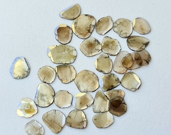 May include: A collection of 20+ raw, unpolished, light brown, and gray diamonds. The diamonds are faceted and have a rough, natural look.