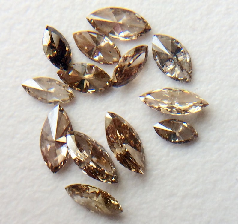 May include: A collection of 14 brown marquise-shaped diamonds. The diamonds are arranged in a random pattern on a white surface.
