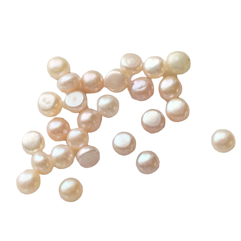 May include: A scattering of off-white round pearls, some with a slight pink hue, on a white background.