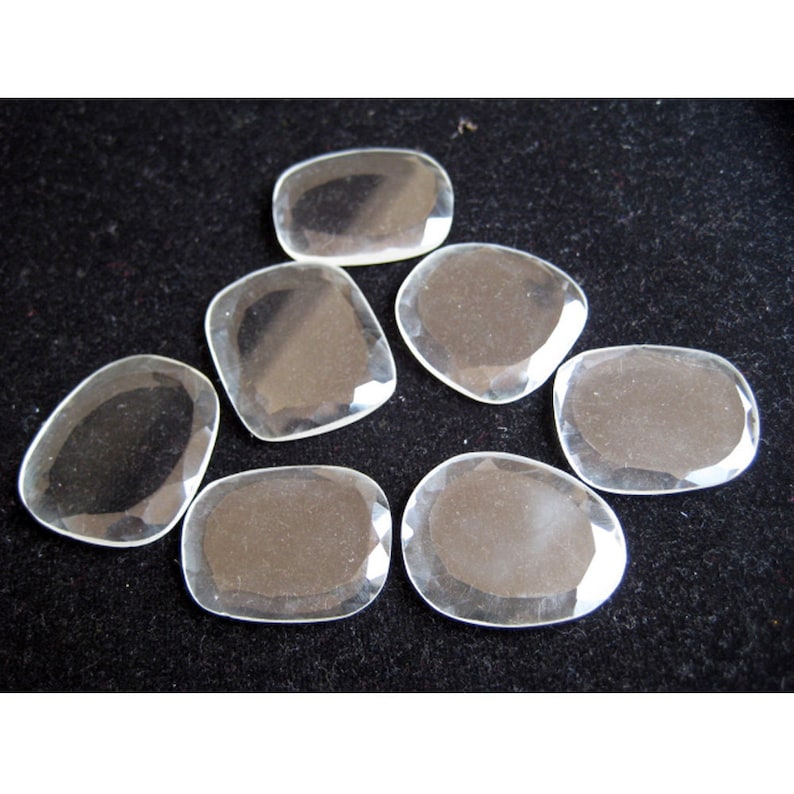 May include: Seven clear, faceted, oval-shaped crystal stones on a black background.
