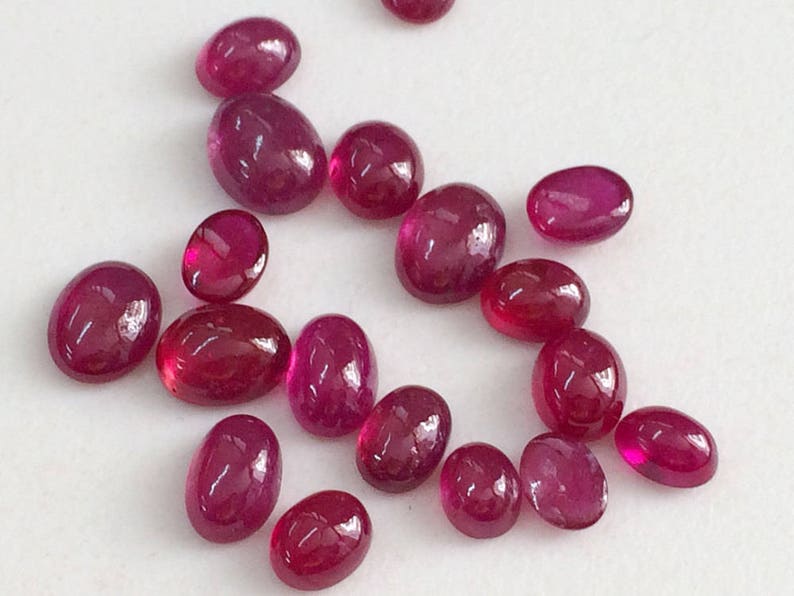 May include: A collection of oval-shaped, polished ruby gemstones in various sizes. The rubies are a deep red color and have a glossy finish.