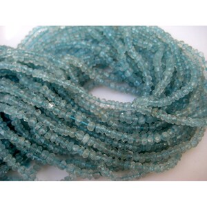 May include: A strand of light blue aquamarine beads. The beads are faceted and have a slightly irregular shape. The beads are strung on a clear thread.