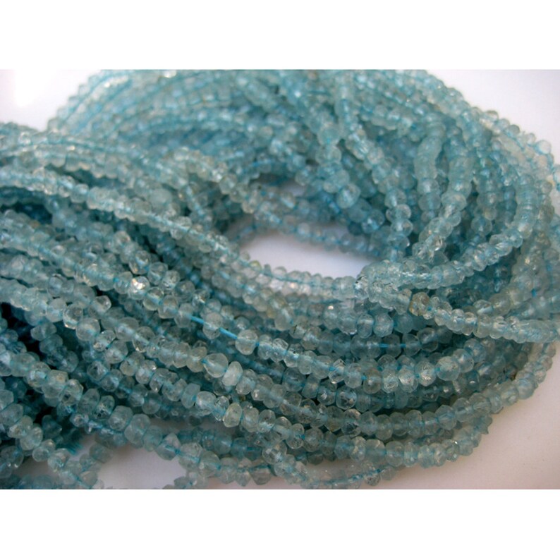 May include: A strand of light blue aquamarine beads. The beads are faceted and have a slightly irregular shape. The beads are strung on a clear thread.