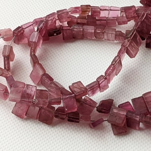 May include: A strand of pink square-shaped gemstone beads. The beads are translucent and have a slight shimmer.