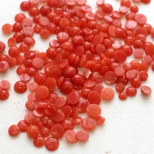 Peut inclure: Un grand tas de petits cabochons de corail ronds. Les cabochons sont d'une couleur rouge orangé vibrante et ont une surface lisse et polie.