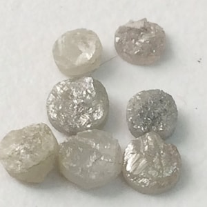 Peut inclure: Sept diamants ronds, gris, taillés en brut. Les diamants sont tous approximativement de la même taille et de la même forme.