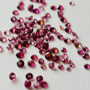 Op de afbeelding: Een verzameling losse roze en rode edelstenen, waarschijnlijk robijnen of toermalijnen, verspreid over een wit oppervlak.