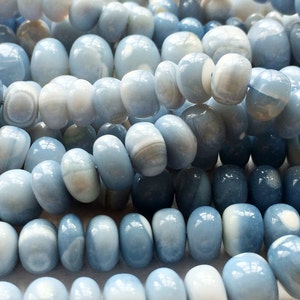 May include: A strand of light blue and white agate beads. The beads are smooth and polished, with a slightly oval shape. The beads are strung on a clear thread.