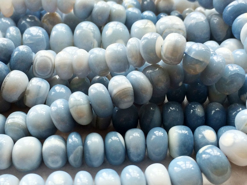 May include: A strand of light blue and white agate beads. The beads are smooth and polished, with a slightly oval shape. The beads are strung on a clear thread.